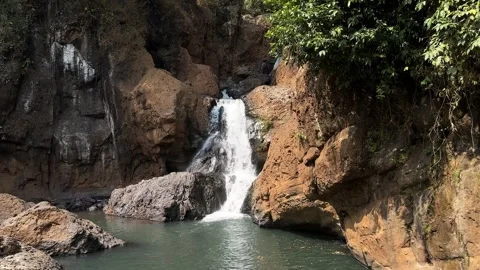 Waterfall Cascading into Pool, Rocky Cliff, Lush Greenery, Downward Pan Stock Footage 324769214
