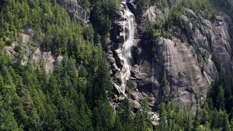 Waterfall cascading off the side of a granite cliff covered with evergreens. Video stock 111947984