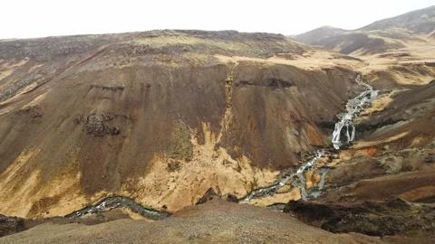 Waterfall cascading through volcanic hills on an overcast day in Reykjadalur Stock Footage 339303814