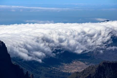 A waterfall of clouds flowing over a mountain range into a valley. Background Stock Photos