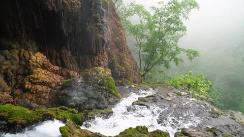 A waterfall is coming down a rocky cliff in a foggy forest Stock Footage 268405034