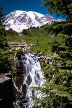 Waterfall crashes down in front of the snow capped Mount Rainier Stock Photos