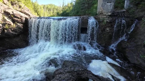 Waterfall crashing over rocks below the ruins of a historic mill dam. Video stock 344462443