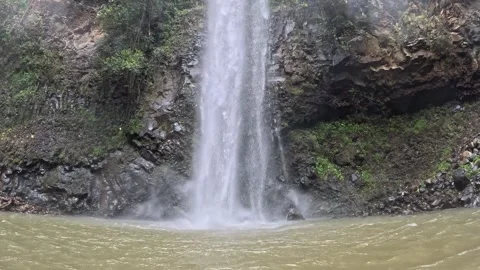 Waterfall dropping over a rock wall into a green pool in Hawaii 動画素材 348405421