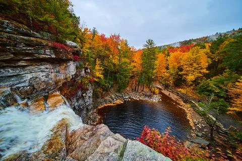 Waterfall at edge dropping into river below and surrounded by stunning fall Stock Photos