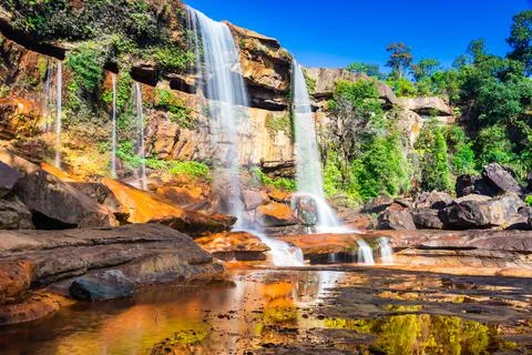 Waterfall falling from mountain top with reflection and blue sky at morning f 스톡 사진