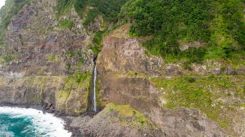 Waterfall falling into ocean from volcanic cliffs. Stock Photos