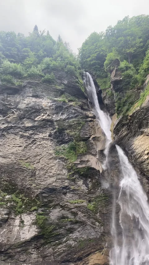 A waterfall falls down from a rocky mountain into a valley flows 動画素材 314783771