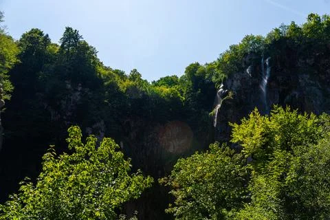 Waterfall flowing down a steep rocky cliff surrounded by dense green forest.. 스톡 사진
