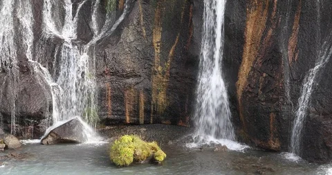 The waterfall flows down the cliff into the blue water Stockbeeldmateriaal 95750093
