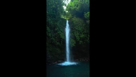 Waterfall flows down a cliff into a pool. Ideal for tranquil nature scenes Vídeos de archivo 334628384