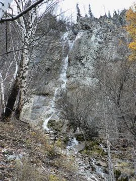 Waterfall flows down from the cliff. Trees on each side Stock Photos