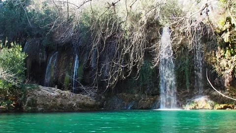 The waterfall flows down the mountain into a turquoise mountain lake. A rainbow Stock Footage 247186166