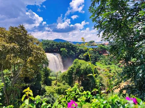 Waterfall flows into green valley under blue sky with clouds in the afternoon Stock Photos