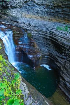 The waterfall flows into a moss-covered pool surrounded by rocks and plants.. Foto stock