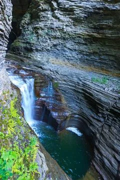The waterfall flows into a moss-covered pool surrounded by rocks and plants.. Stock Photos