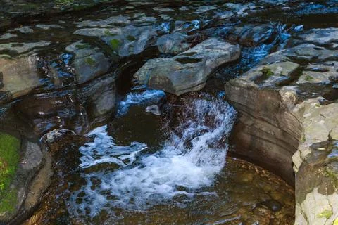 The waterfall flows into a moss-covered pool surrounded by rocks and plants.. Foto stock