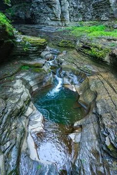 The waterfall flows into a moss-covered pool surrounded by rocks and plants.. 스톡 사진