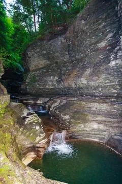 The waterfall flows into a moss-covered pool surrounded by rocks and plants.. Stock Photos