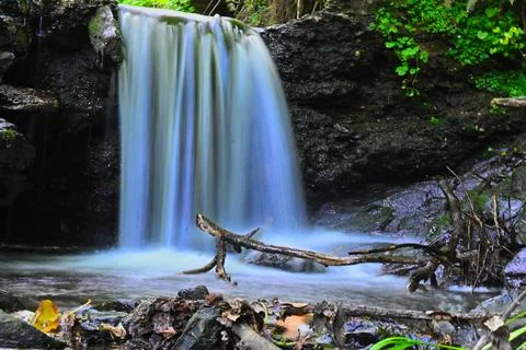 Waterfall flows over rocks in a forest setting during daytime with green pl.. Stock Photos