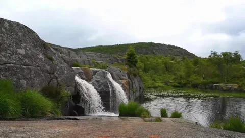 Waterfall flows over rocks in Norway near a calm lake surrounded by green h.. Stock Footage 340213264