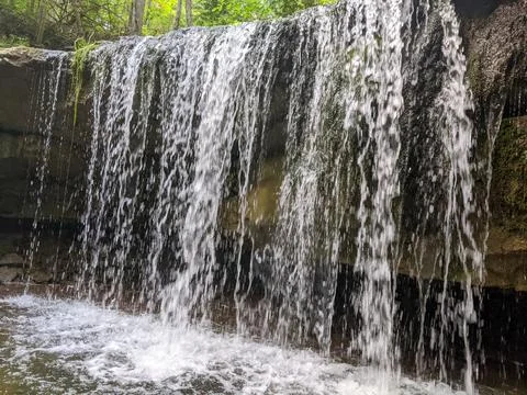 A waterfall flows over a stone cliff in a forest Stock Photos