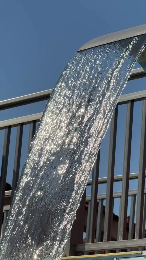 A waterfall flows into a spa pool under the open sky, creating a relaxing and 動画素材 302470446
