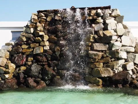 A waterfall flows from a stone wall, falling into a turquoise pool. Decorative Stock Photos