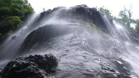 The waterfall flows from the top of the mountain rock creating drizzling Stock Footage 260765494