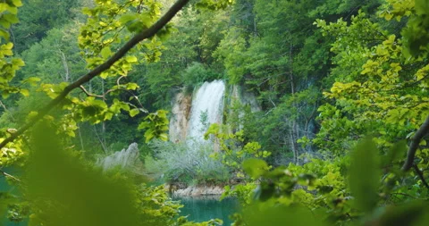 Waterfall flows into turquoise lake surrounded by green trees in Plitvice Lakes Video stock 313305738
