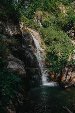 A waterfall is in a forest, surrounded by trees and rocks Stock Photos
