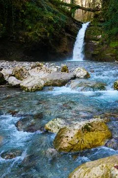 Waterfall in a green spring forest surrounded by stones, clear turquoise wate Foto stock