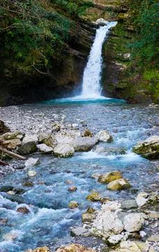 Waterfall in a green spring forest surrounded by stones, clear turquoise wate Fotos de archivo