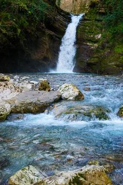 Waterfall in a green spring forest surrounded by stones, clear turquoise wate Stock Photos