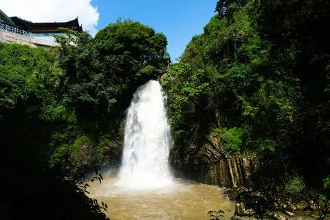 Waterfall in lush forest with cliffside temple Stock Photos