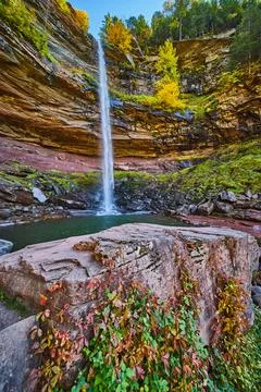 Waterfall pouring over layered cliffs from below with rocks with red and green Stock-Fotos