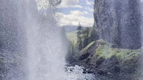 A waterfall pours in the foreground in a small canyon Stock Footage 251925034