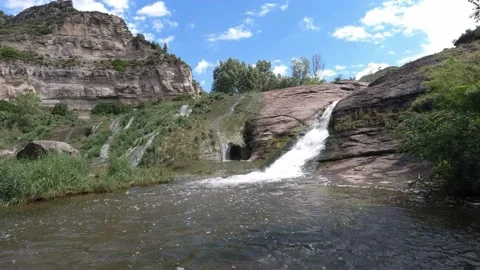Waterfall in a river in a mountainous landscape on a blue sky day Stock Footage 132867178