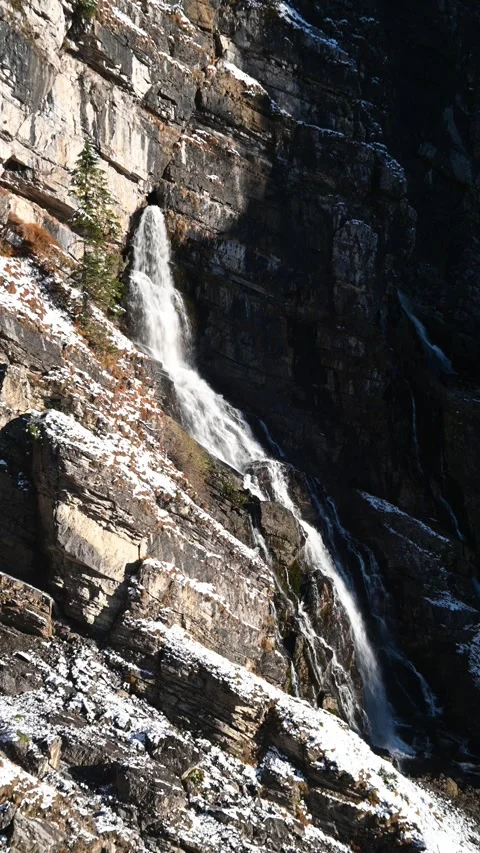 A waterfall runs from a cave in the mountains, first snow in autumn, vertical Video stock 260873515