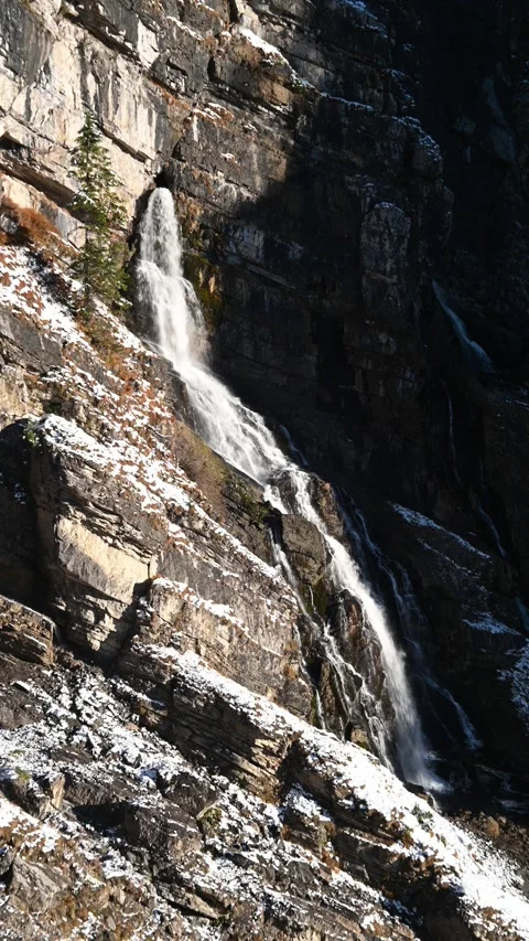 A waterfall runs from a cave in the mountains, first snow in autumn, vertical Video stock 260873600