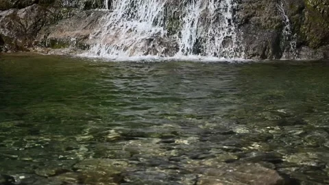 A waterfall runs into a pool in the sunshine (slow motion) Video stock 219645089