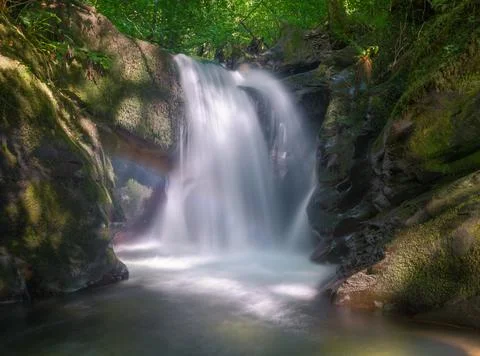 A waterfall with a small rainbow erodes the limestone cliffs Stock Photos