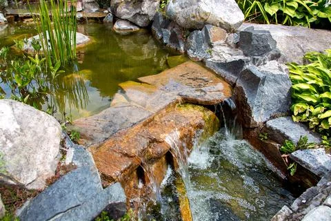 Waterfall on stone artificial pond with flow water in the park on a day. Stock Photos