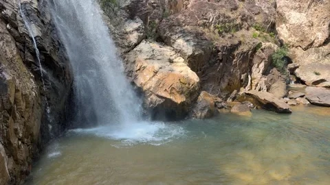 A waterfall stream drops into a natural rock basin at a cliff base forming a qui Stock Footage 338001728