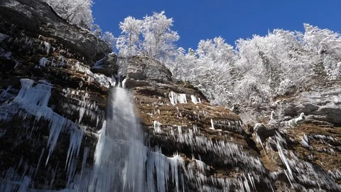 Waterfall under a canopy of trees covered in fresh snow on a sunny winter day Stock Footage 118972560