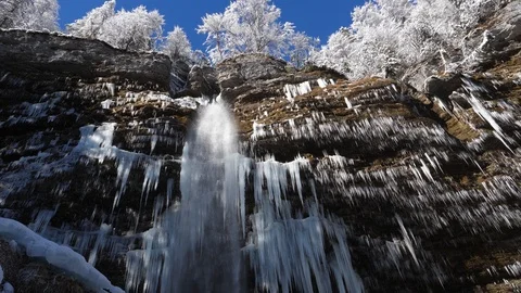 Waterfall in winter falling from the side of a mountain cliff covered in icicles Stock Footage 118971938