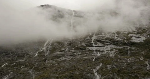 Waterfalls fall down the cliff edges of Milford Sound in New Zealand Stock Footage 120371613