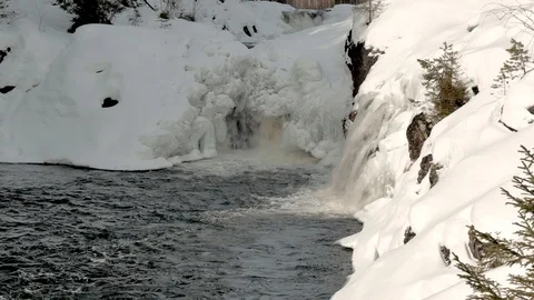Waterfalls fall into small bay surrounded by snowy banks Video stock 108839733