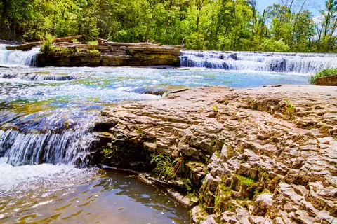 Waterfalls through river with bumpy rocks and green forest Stock Photos