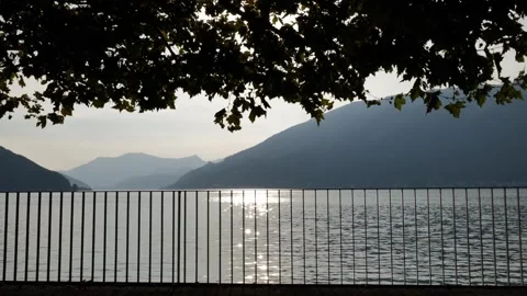 Waterfront with Railing and Tree Branch over Lake Lugano with Mountain in Sunset 動画素材 264476315